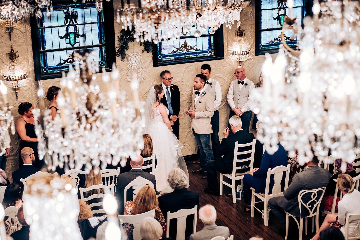 Wedding ceremony photographed through crystal chandelier decorations in an elegant venue.