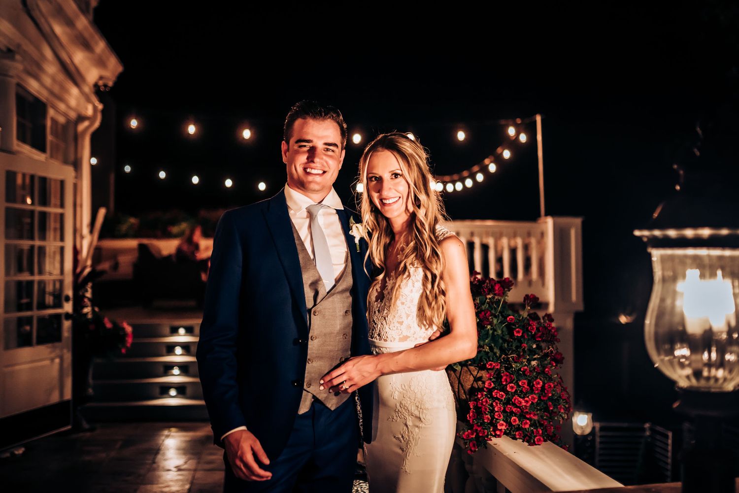 Couple poses for an evening portrait with string lights creating a romantic ambiance.