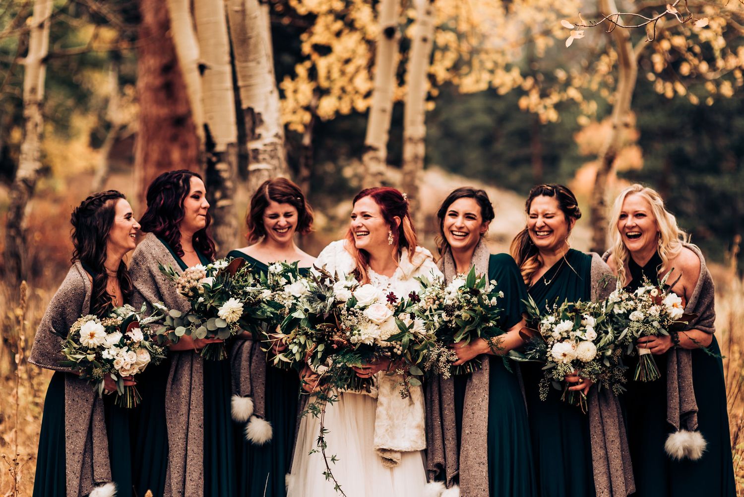 Bridal party with white bouquets poses among autumn trees with golden leaves.