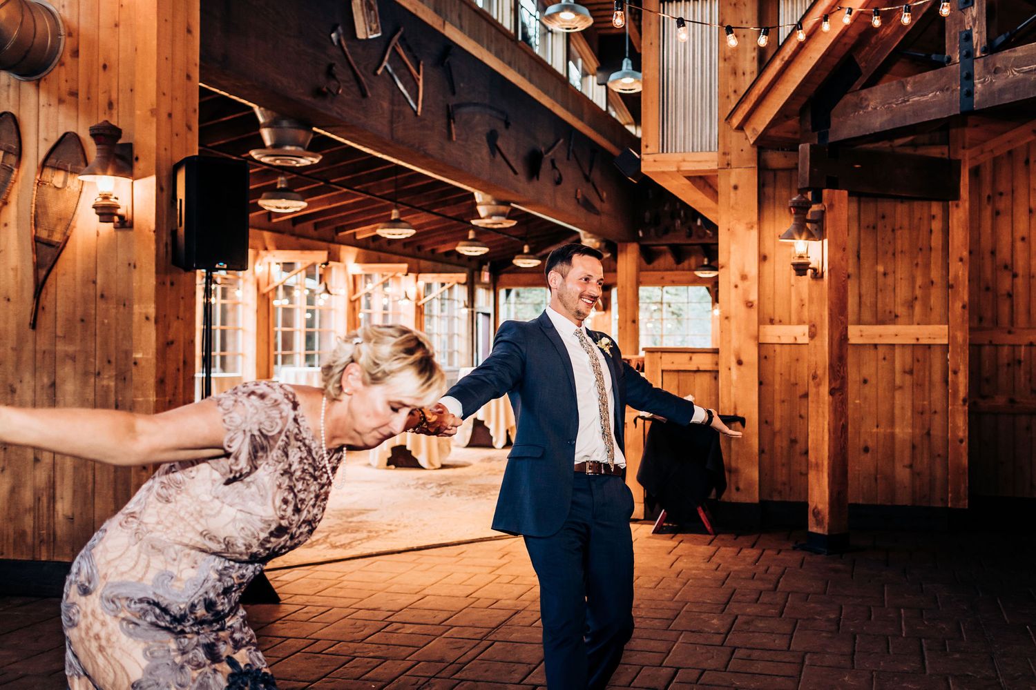 Dancing couple twirls in rustic wooden reception hall with warm lighting.