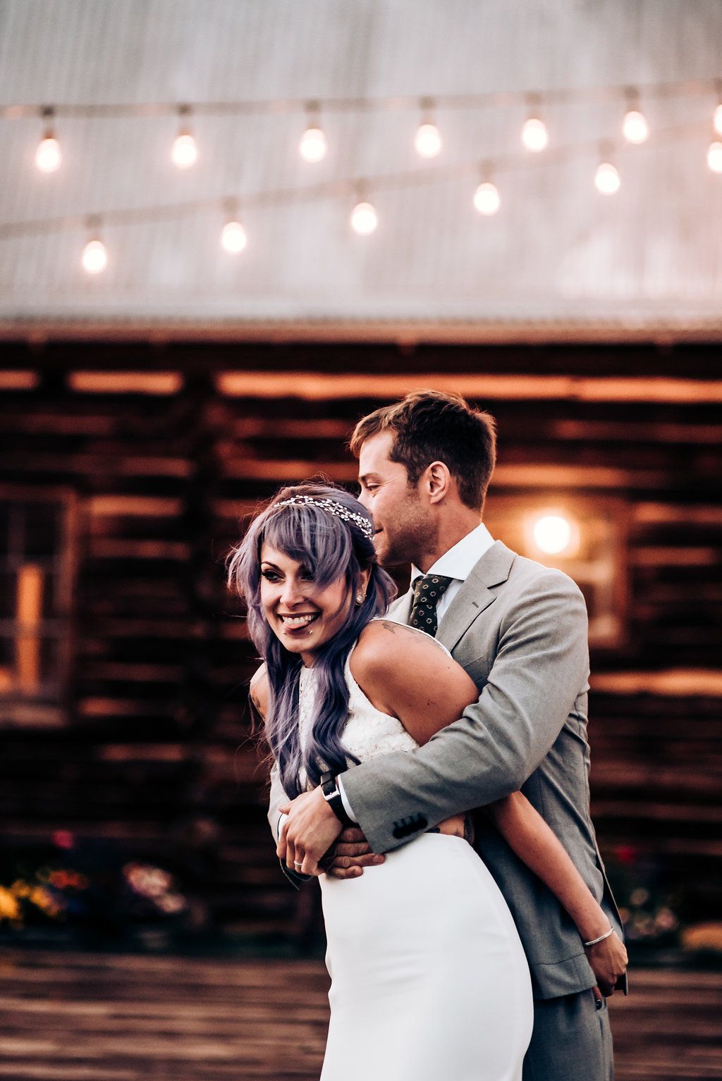 A romantic moment between newlyweds under string lights at a rustic outdoor venue.
