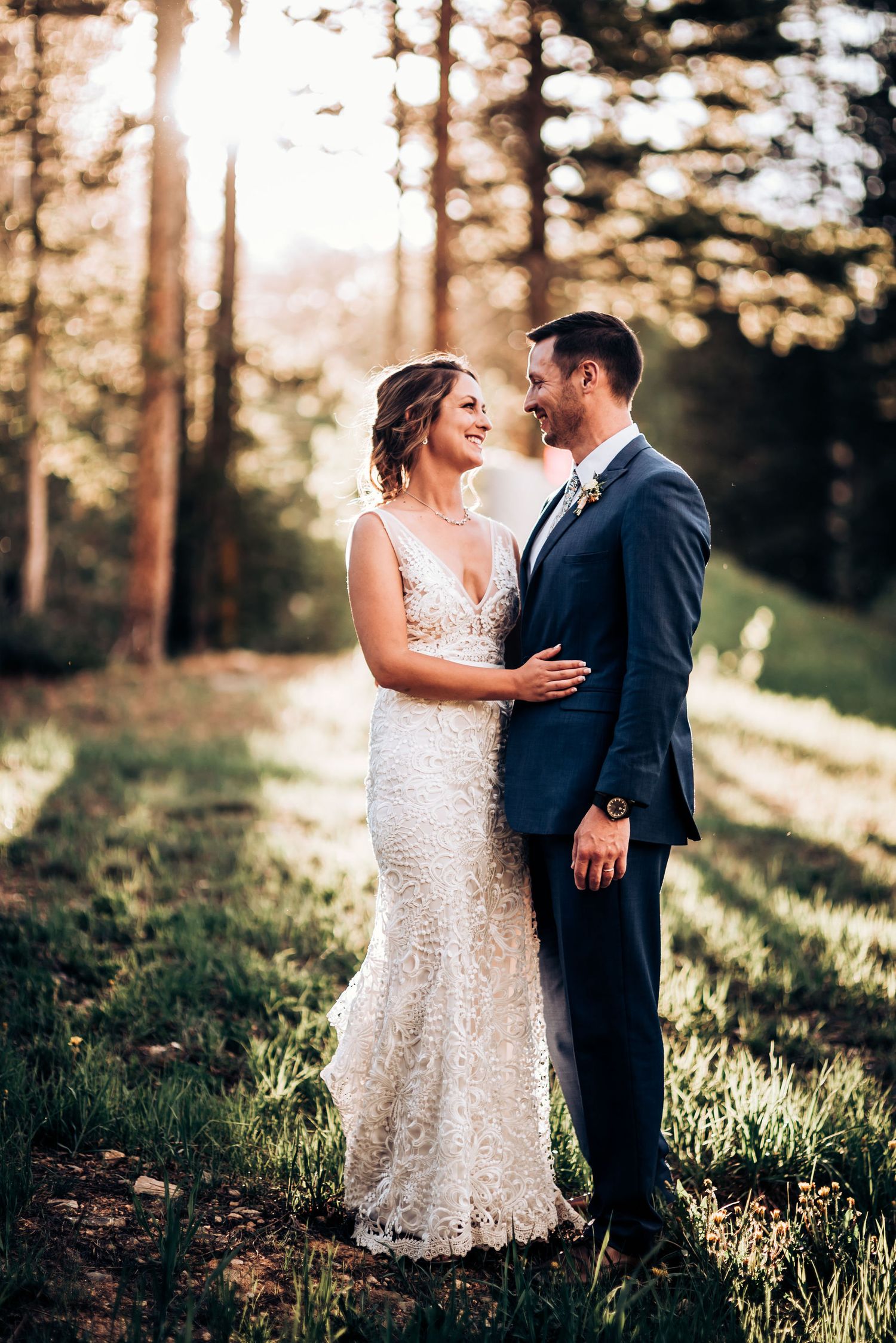Newlyweds share loving moment in sunlit forest clearing during golden hour.