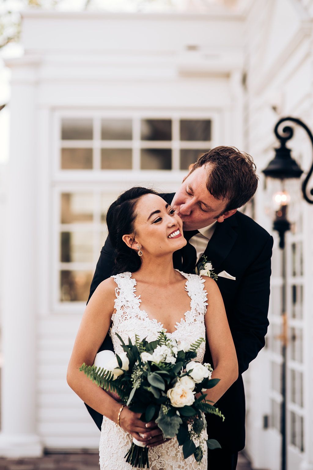 Romantic moment captured between couple against white building exterior.