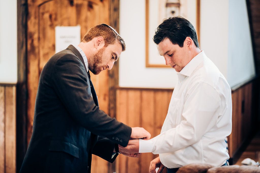 Two men in formal attire prepare for a wedding ceremony in a wooden interior setting.