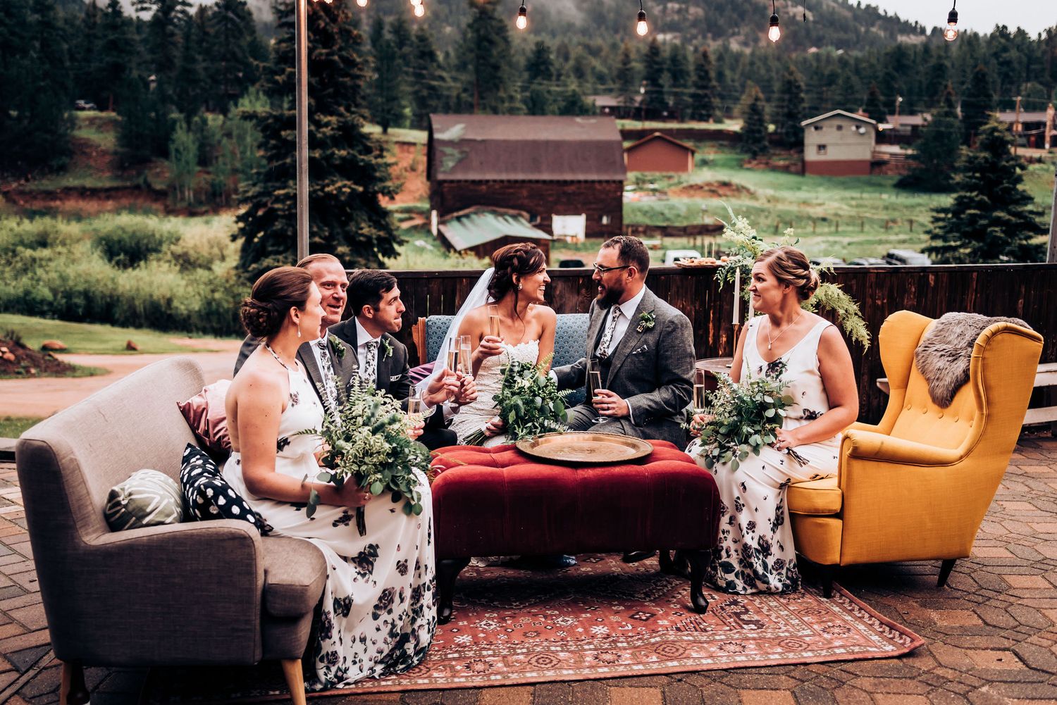 Wedding party relaxes on vintage furniture during outdoor mountain celebration.