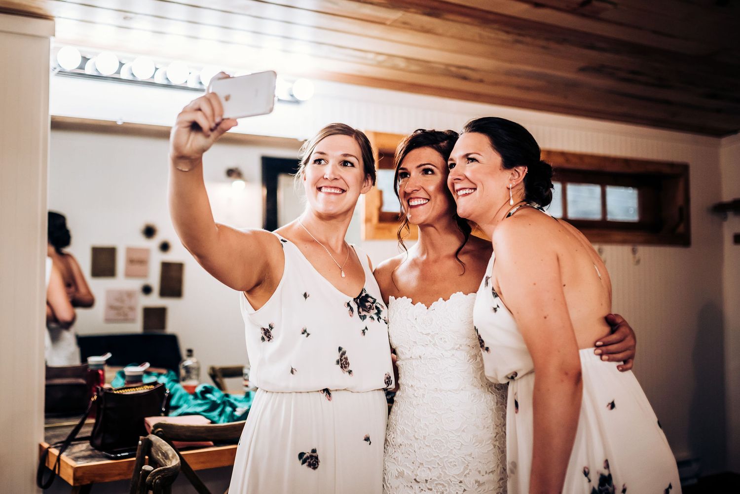 Wedding party members in white dresses taking a selfie together during pre-ceremony preparations.