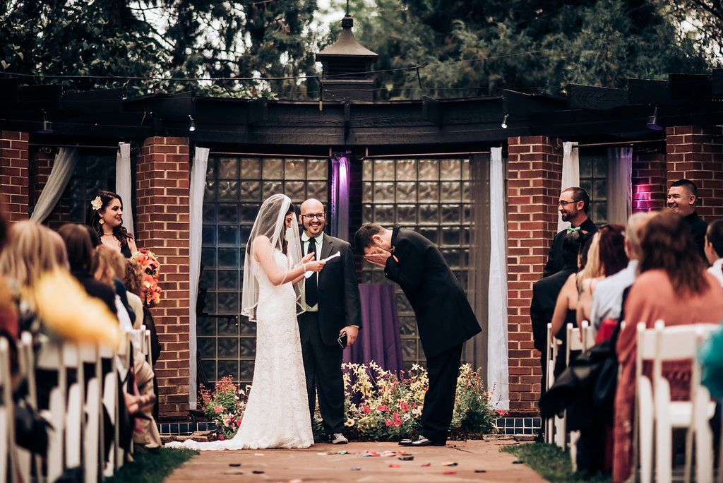 Couple during wedding ceremony at brick pergola venue with seated guests on both sides.