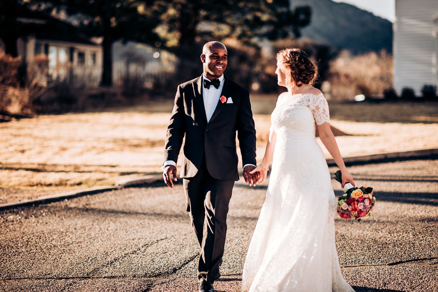 Newlyweds walk hand in hand on paved pathway during golden hour.