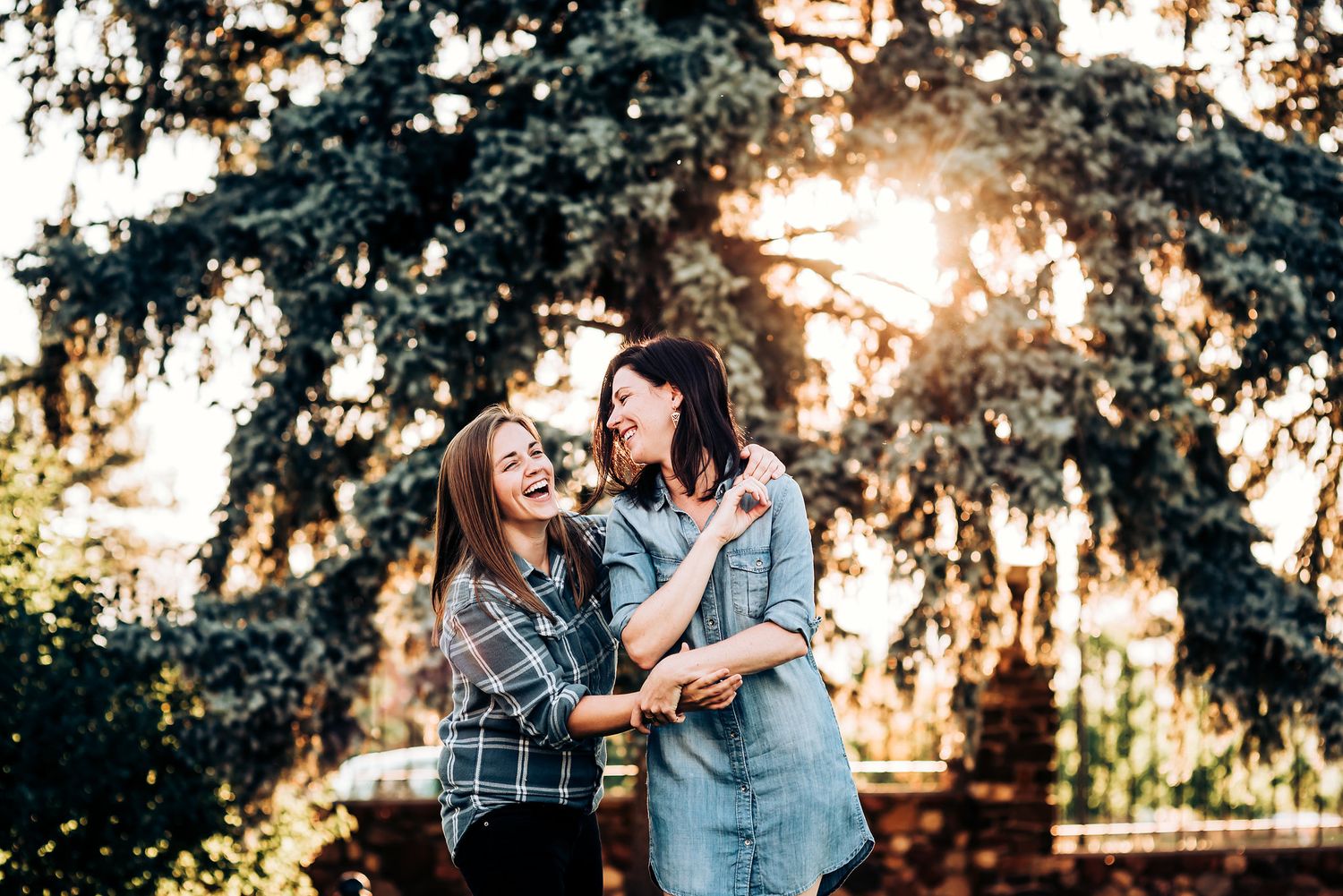 Two people sharing a joyful moment together in a garden with sunlit trees in the background.