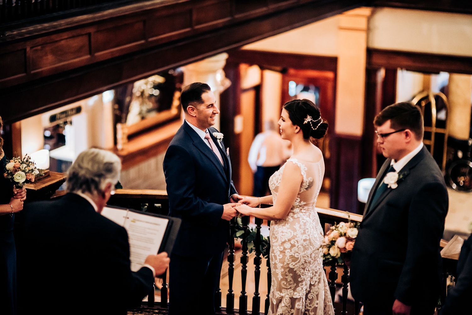 Wedding ceremony on ornate wooden staircase landing with warm ambient lighting.