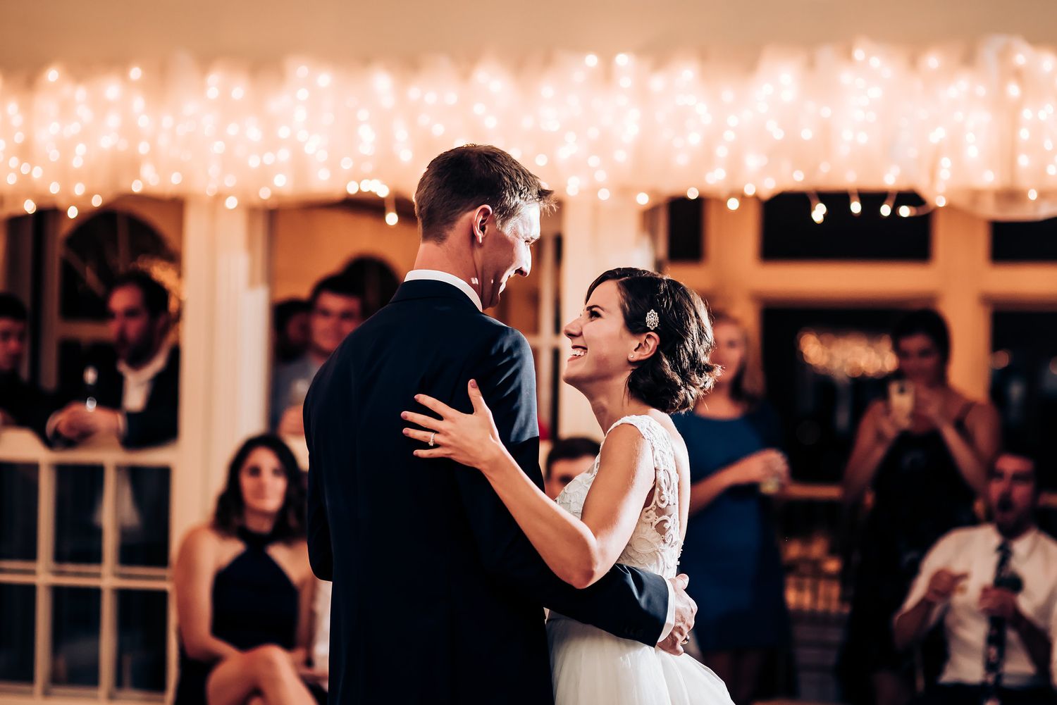 A couple shares their first dance as newlyweds under twinkling lights at their wedding reception.
