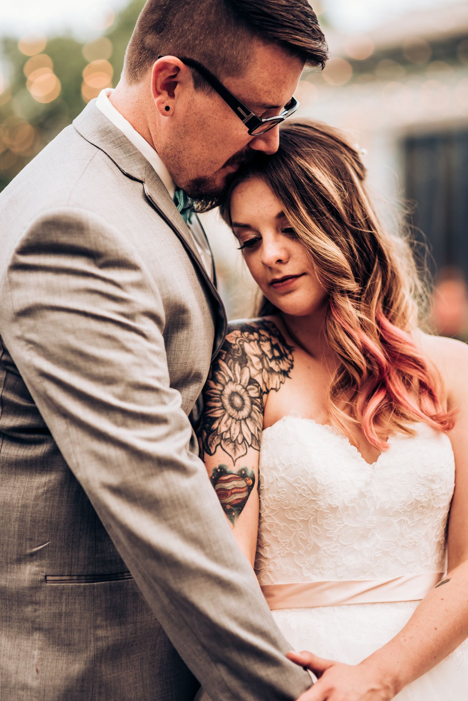Intimate wedding portrait showing tender moment between couple with string lights in background.
