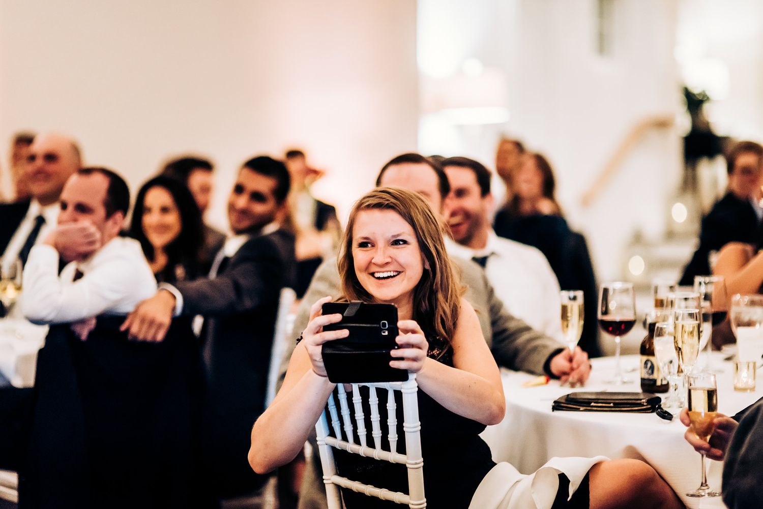 Wedding guests enjoy speeches and toasts during an elegant indoor reception.