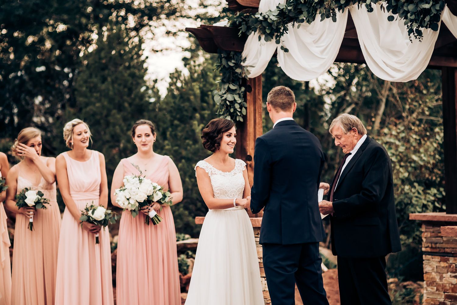 A wedding ceremony in progress with attendants in pink dresses standing to one side.
