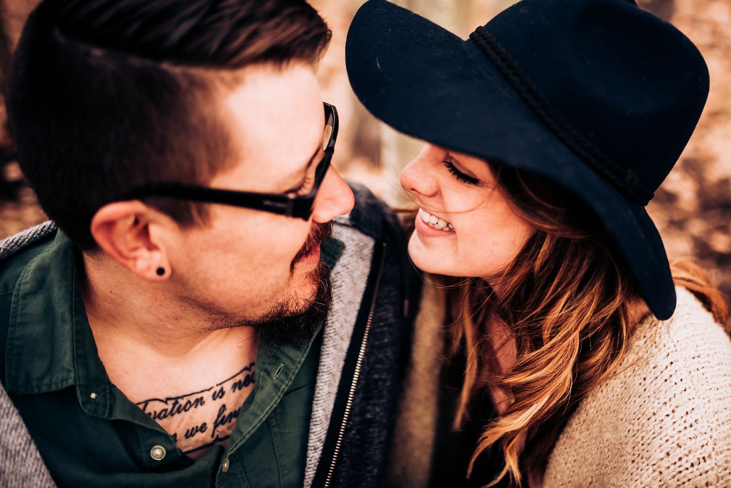A romantic moment between a couple in a hat and glasses sharing a sweet laugh outdoors.