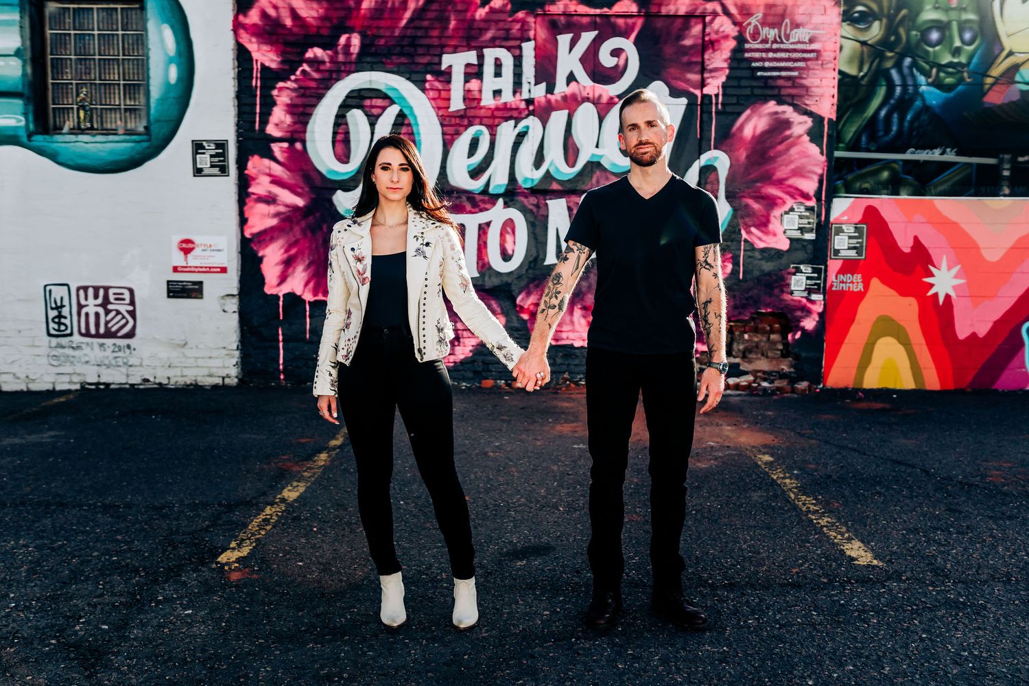 Couple stands casually in front of colorful urban street art backdrop.