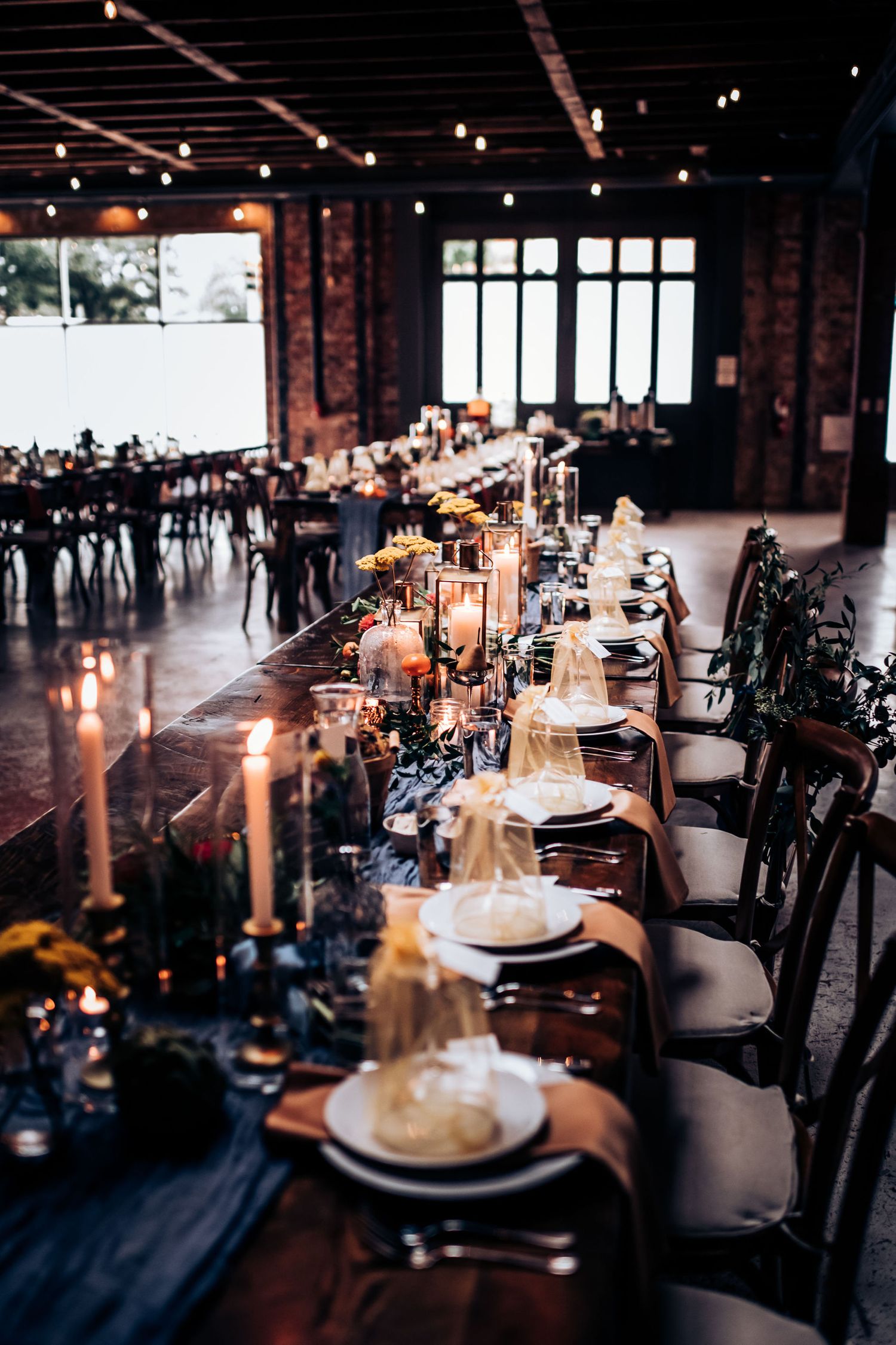 Long reception table with romantic candlelight and place settings in industrial wedding venue.