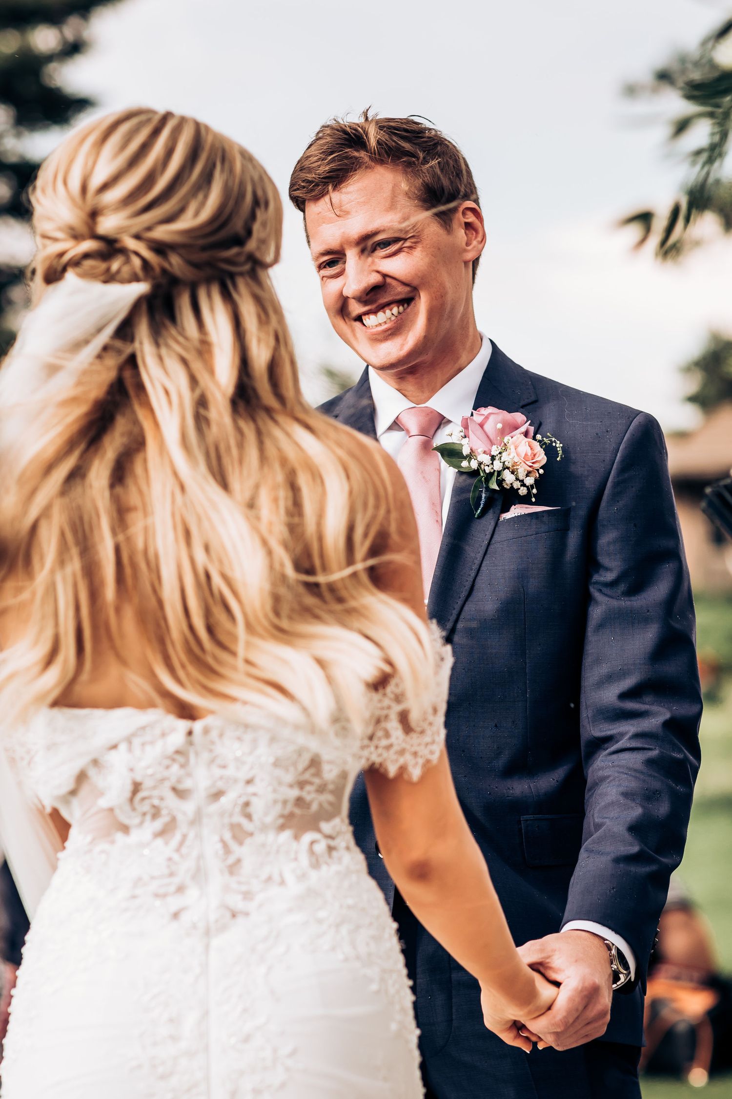 Intimate moment between newlyweds during outdoor wedding ceremony with groom wearing pink tie and boutonniere.