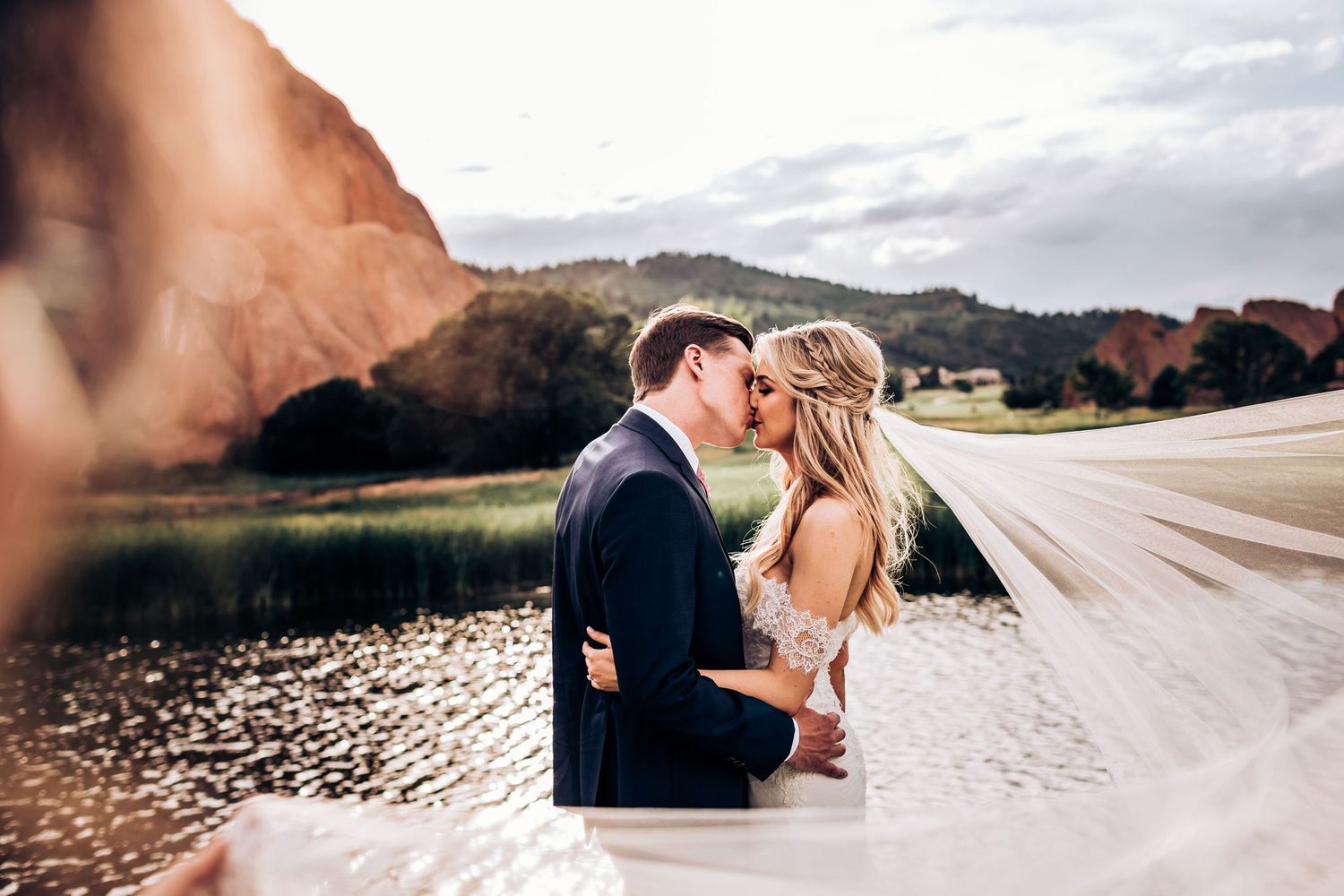 Intimate wedding moment captured with flowing veil against lake and mountain scenery.