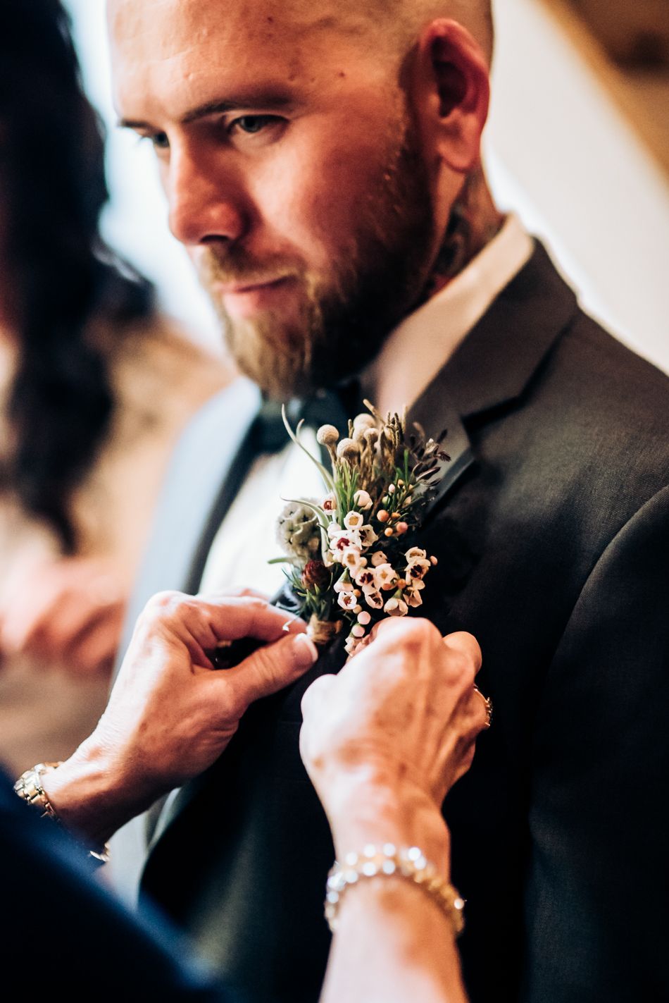 A boutonniere being pinned onto a dark suit jacket during wedding preparations.