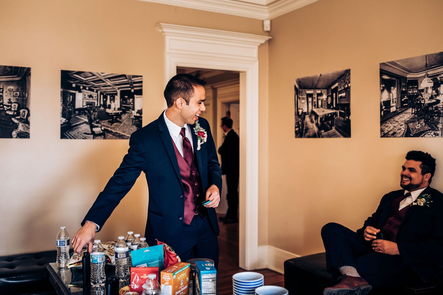 Wedding party members relax in preparation room with drinks and snacks.