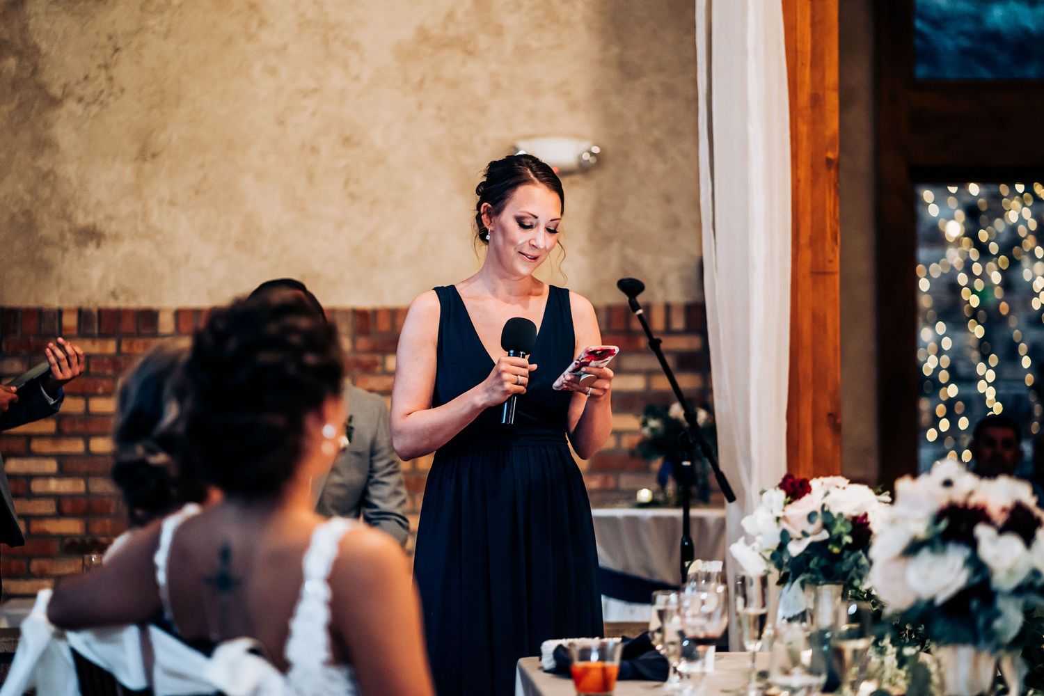 Person in navy dress giving emotional speech at wedding reception.