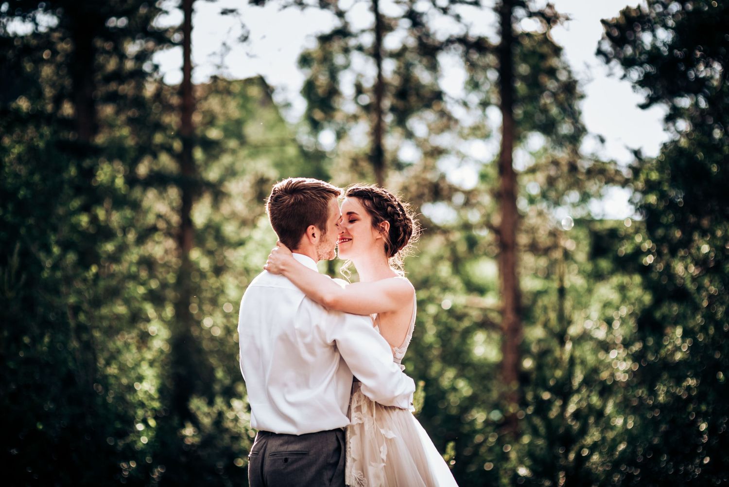 A tender kiss shared between newlyweds in a serene forest setting.