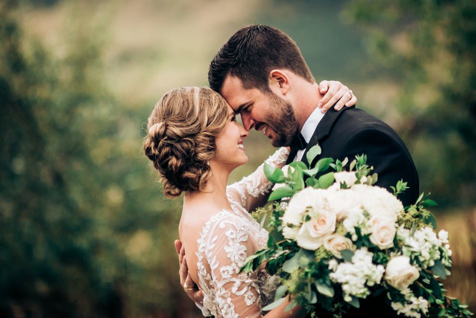 Romantic outdoor wedding portrait with white floral bouquet against natural backdrop.