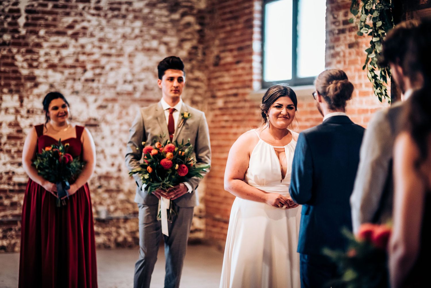 Wedding party standing at altar with burgundy bridesmaid dress and rustic floral arrangements.
