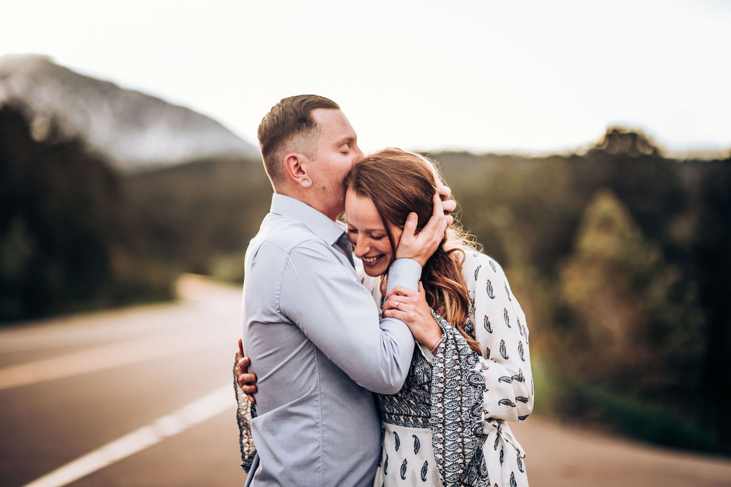 Intimate moment captured between couple on winding mountain road at dusk.