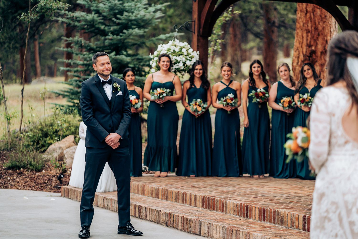 An outdoor wedding ceremony with attendants in navy blue dresses and white floral arrangements.