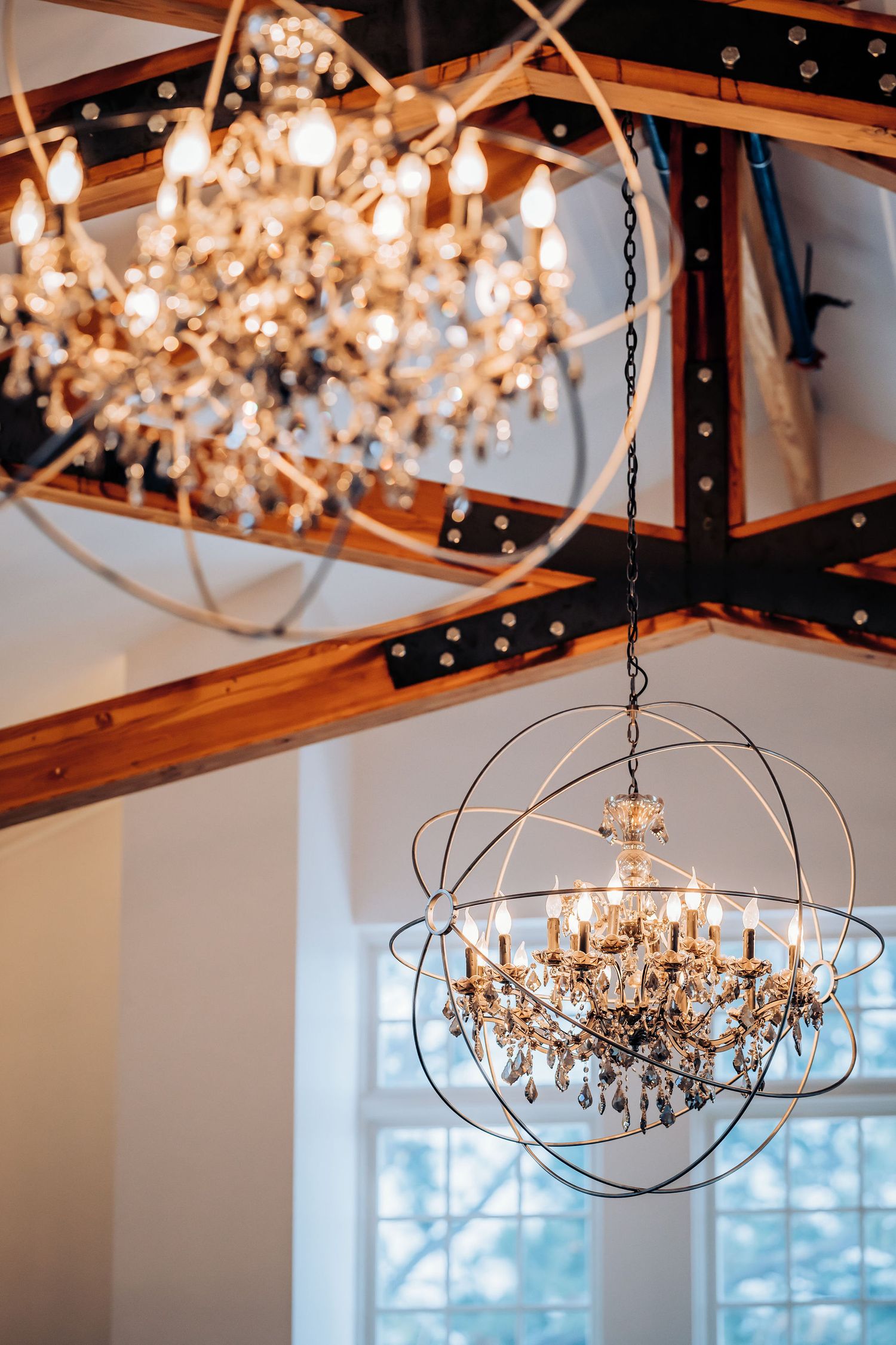 Crystal orb chandeliers hanging from wooden beams in elegant white room.