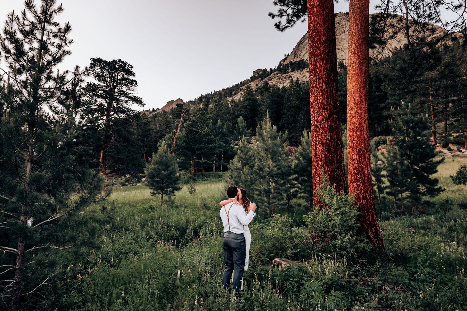 A romantic moment captured between pine trees in a peaceful mountain setting.