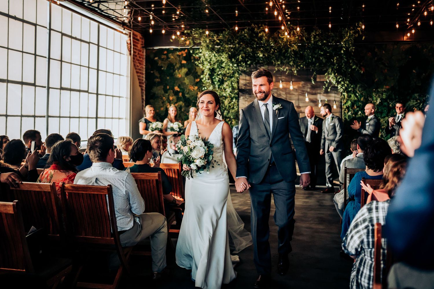 Wedding recessional in industrial venue with exposed brick walls and large windows.