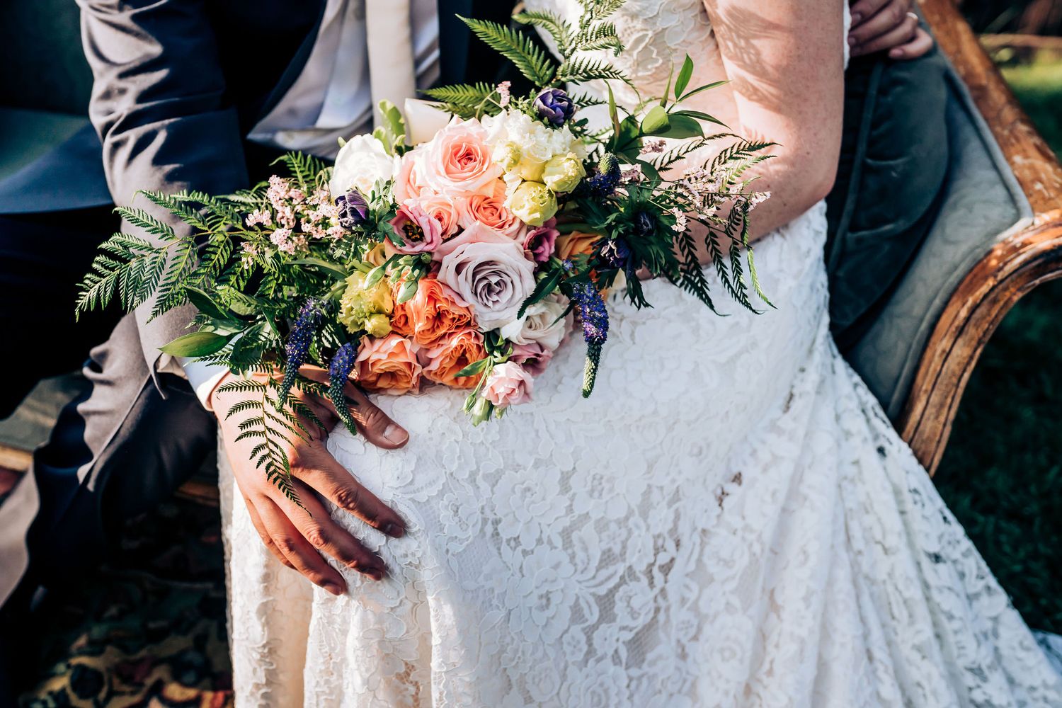 Close-up of bridal bouquet featuring pink roses and greenery with lace wedding dress detail.