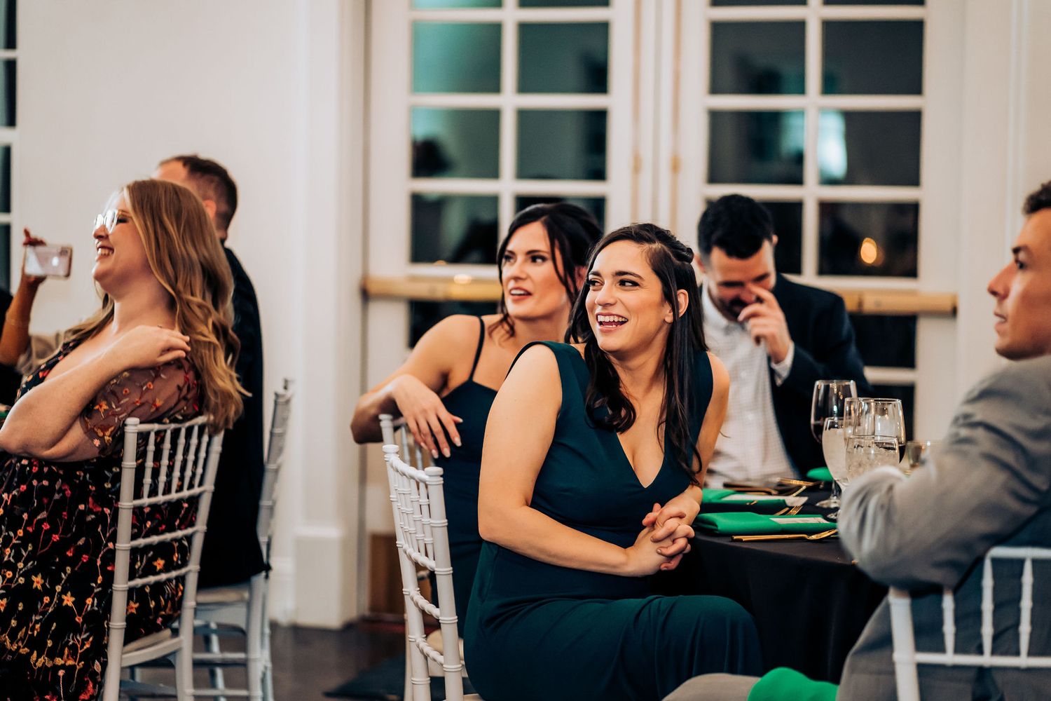 Wedding guests laugh and smile during reception dinner at decorated tables.
