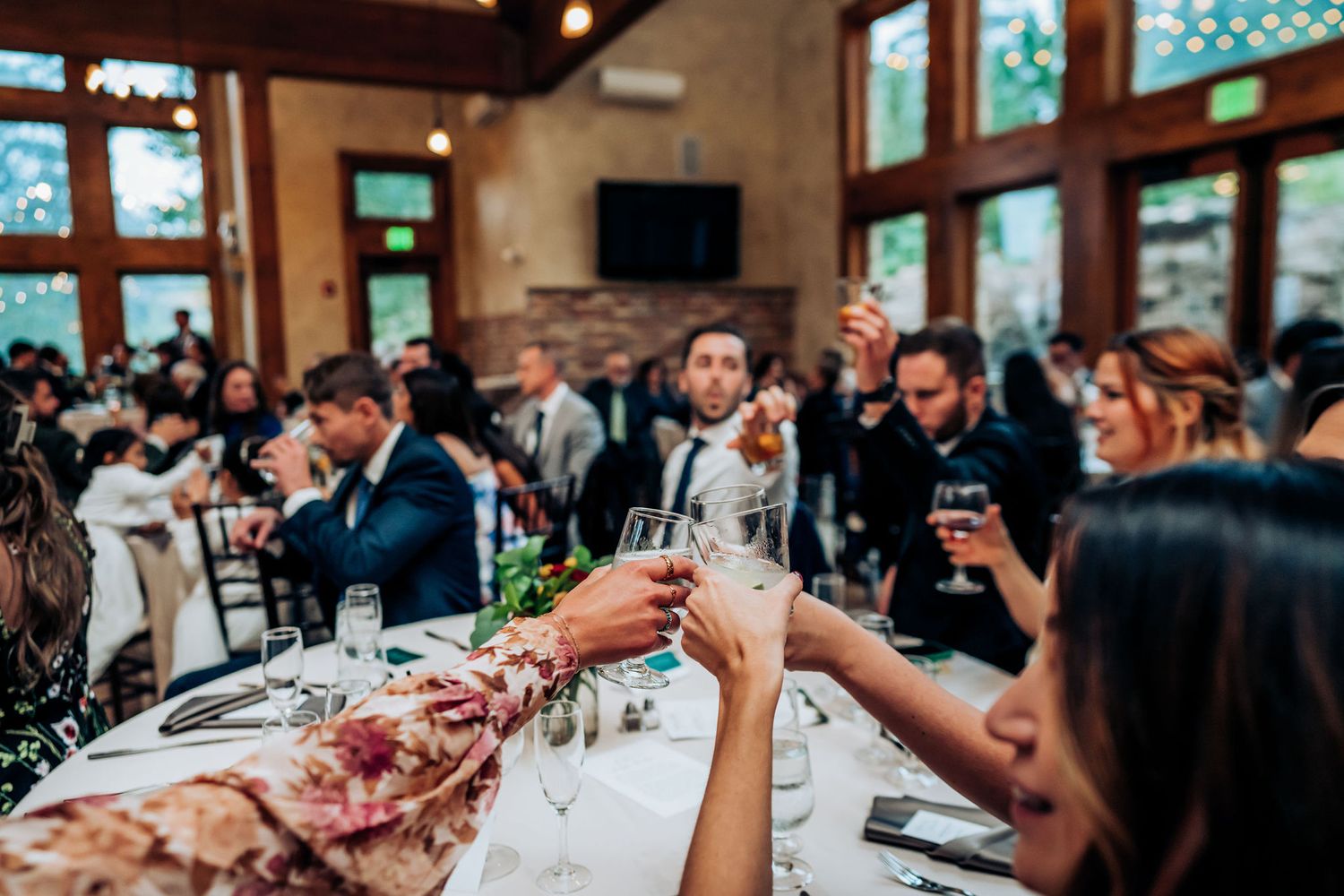 Wedding guests raise their glasses in a celebratory toast at a rustic reception venue.