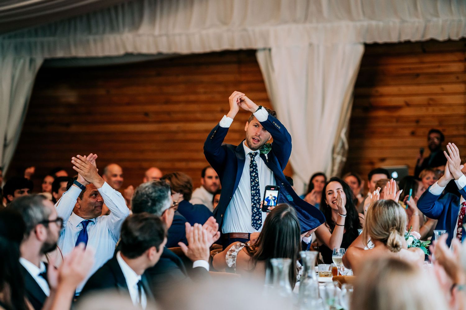 Wedding guests standing and cheering during a celebration at an indoor reception venue.