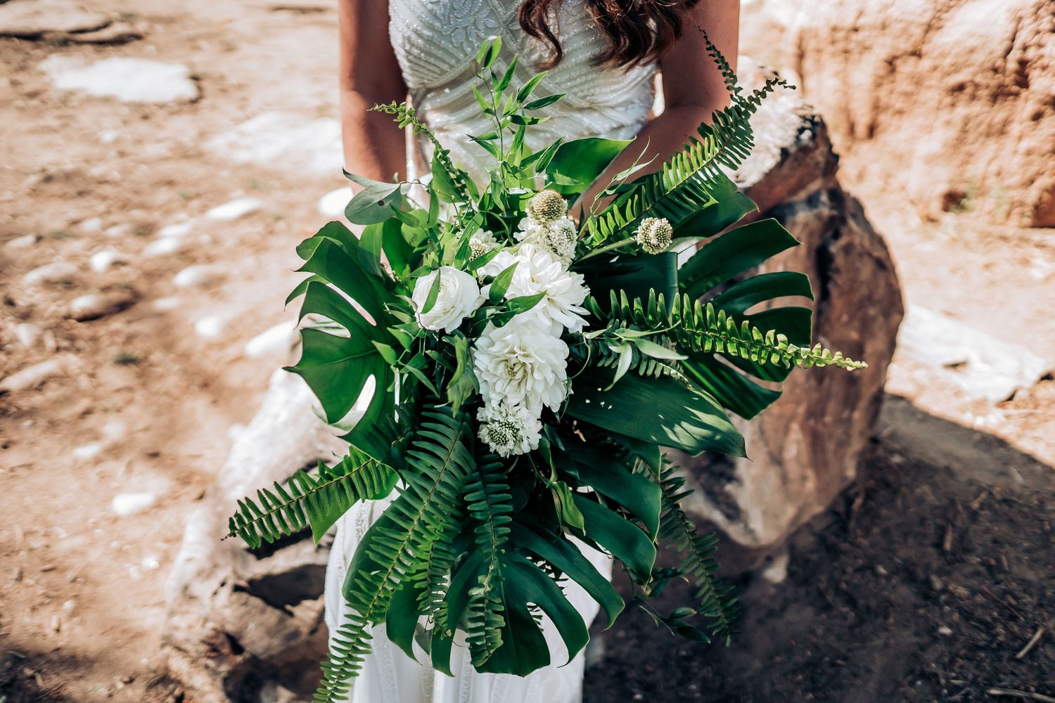 Tropical wedding bouquet featuring large monstera leaves and white flowers against a desert backdrop.