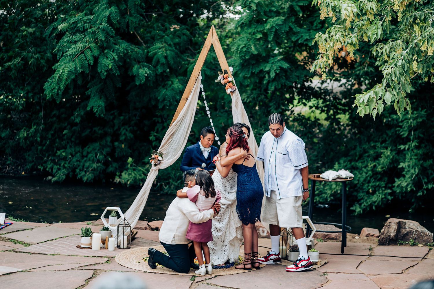 Intimate gathering around a wooden triangle arch during an outdoor ceremony.