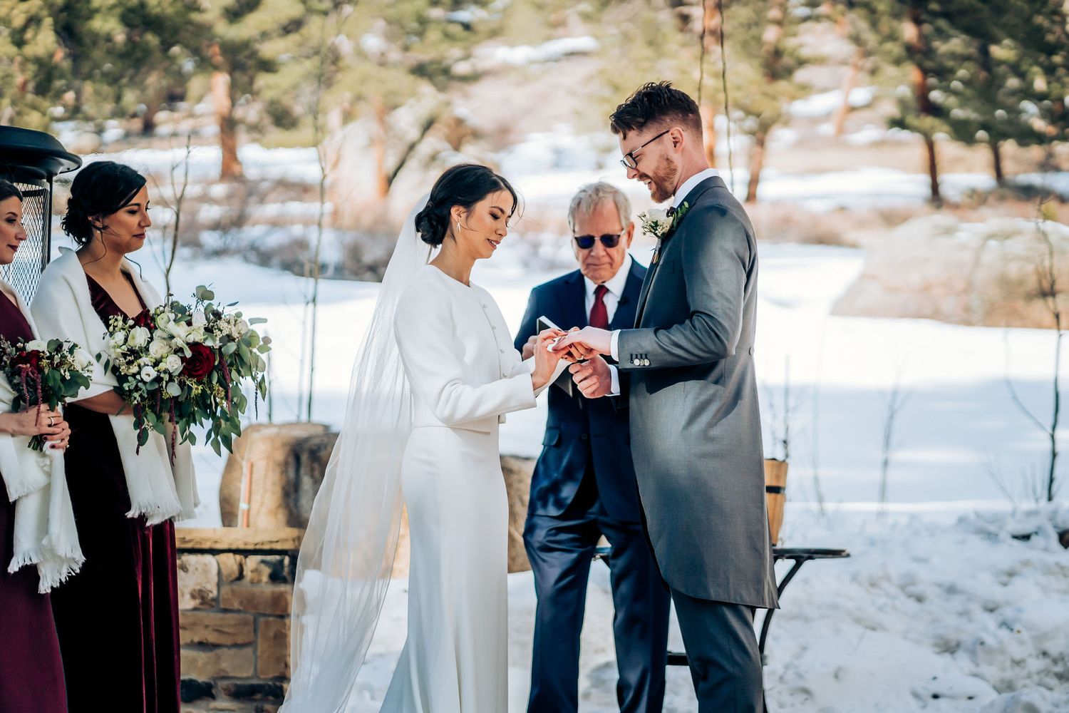 Winter wedding ceremony takes place outdoors with snow in background as couple exchanges rings.
