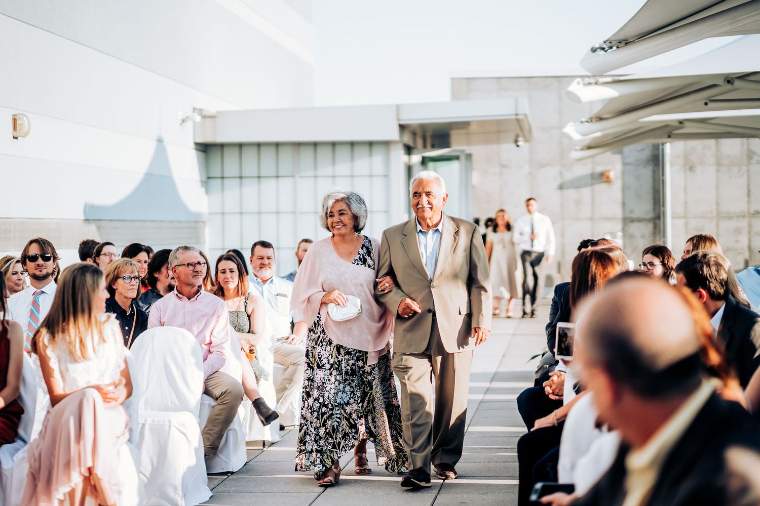 Wedding processional on modern rooftop with guests in white attire watching.