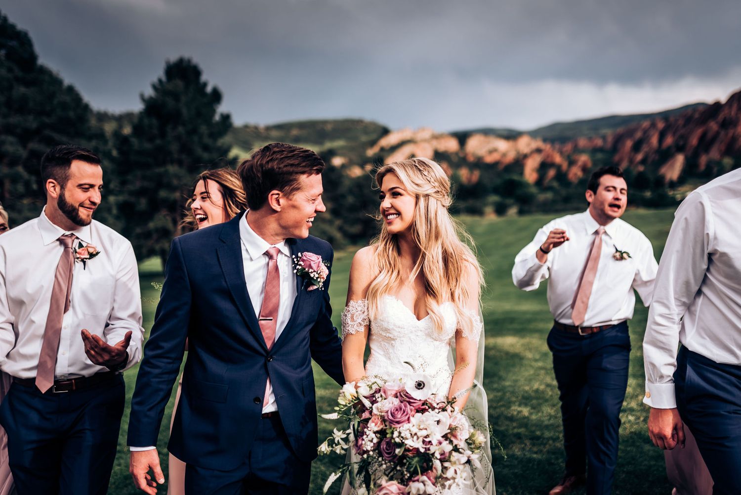 Wedding party shares candid moment outdoors with red rocks in background.