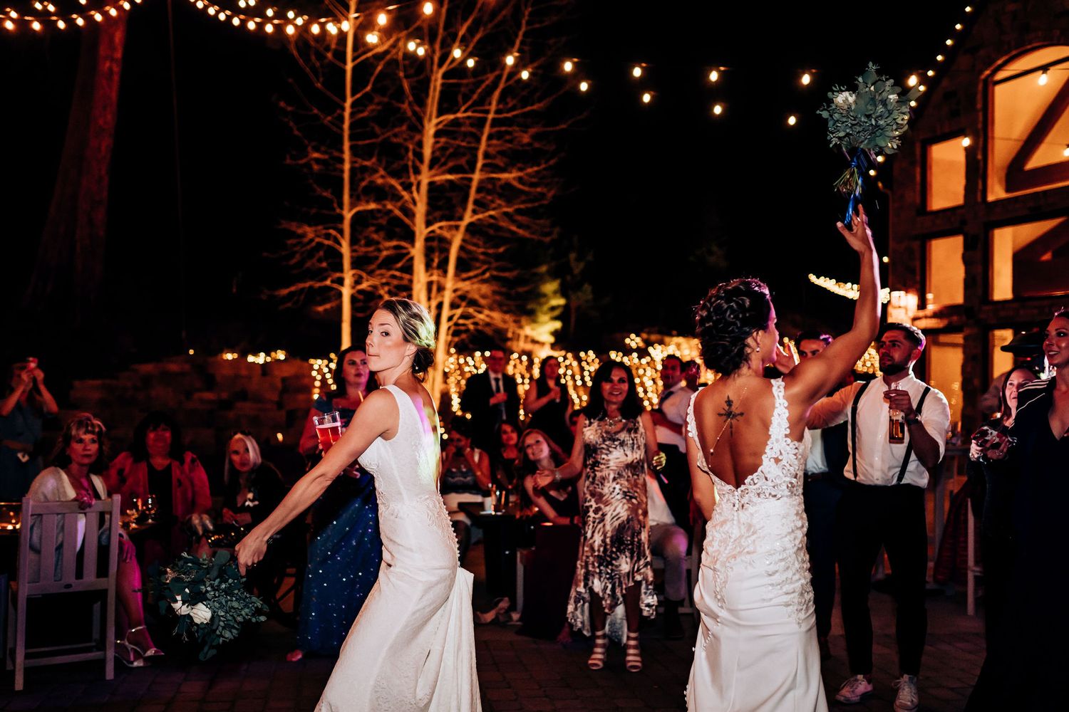 Outdoor wedding celebration with dancing under string lights against a rustic building backdrop.