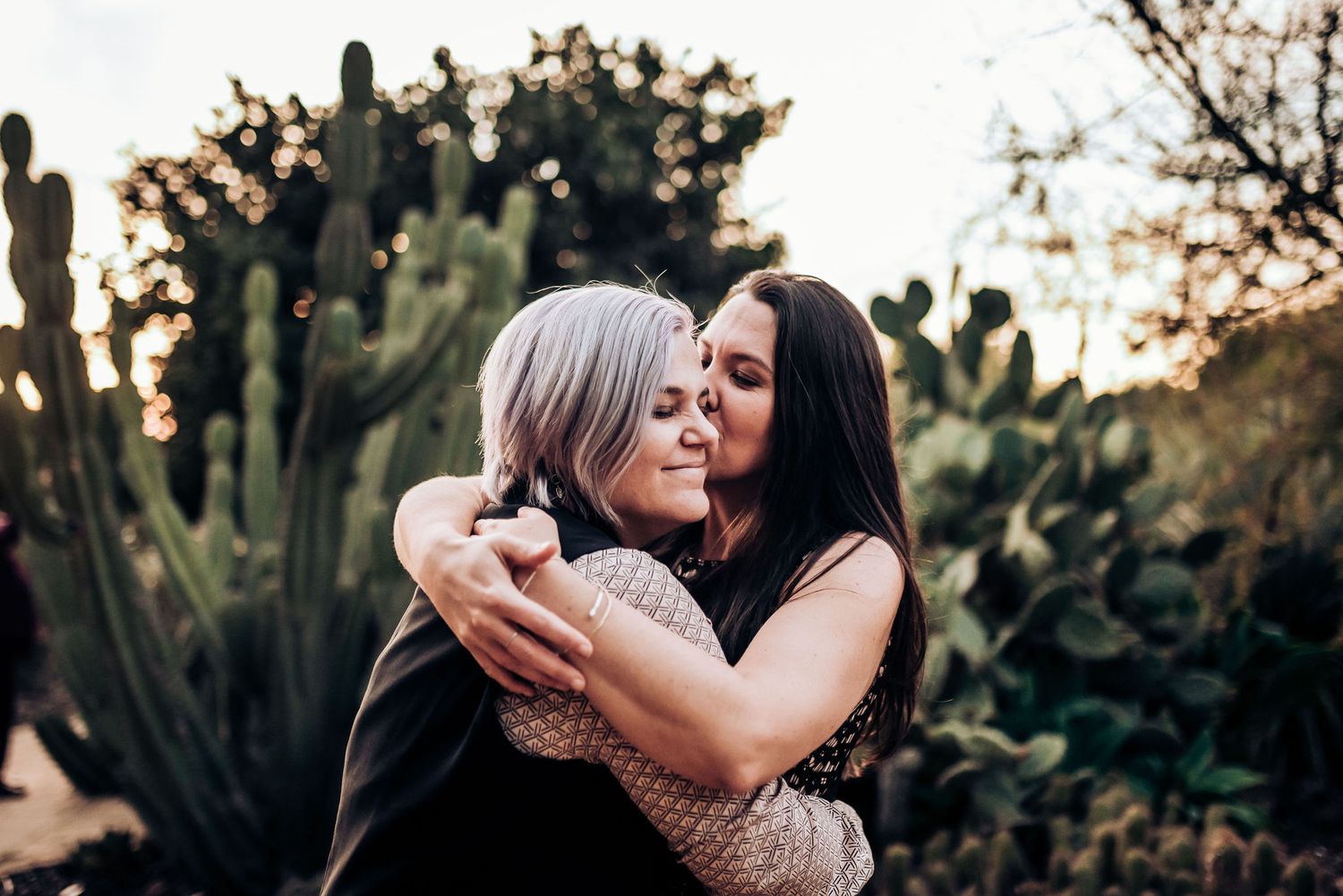 An affectionate embrace captured in a desert garden with cacti in the background.