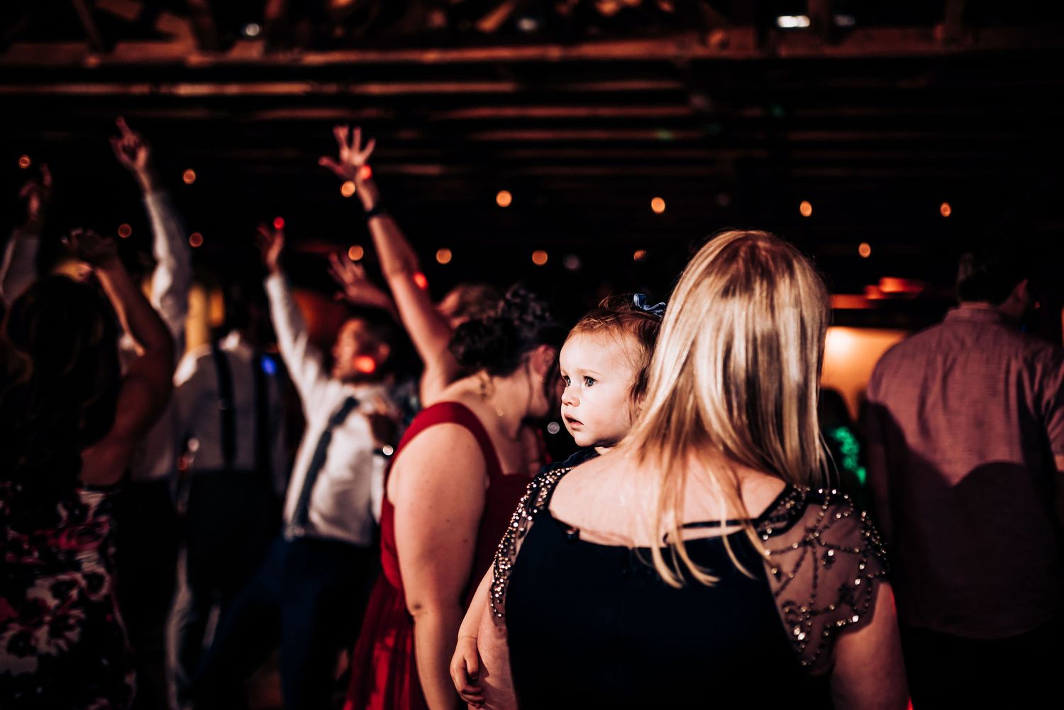 People dancing with hands raised at a lively indoor celebration with string lights overhead.