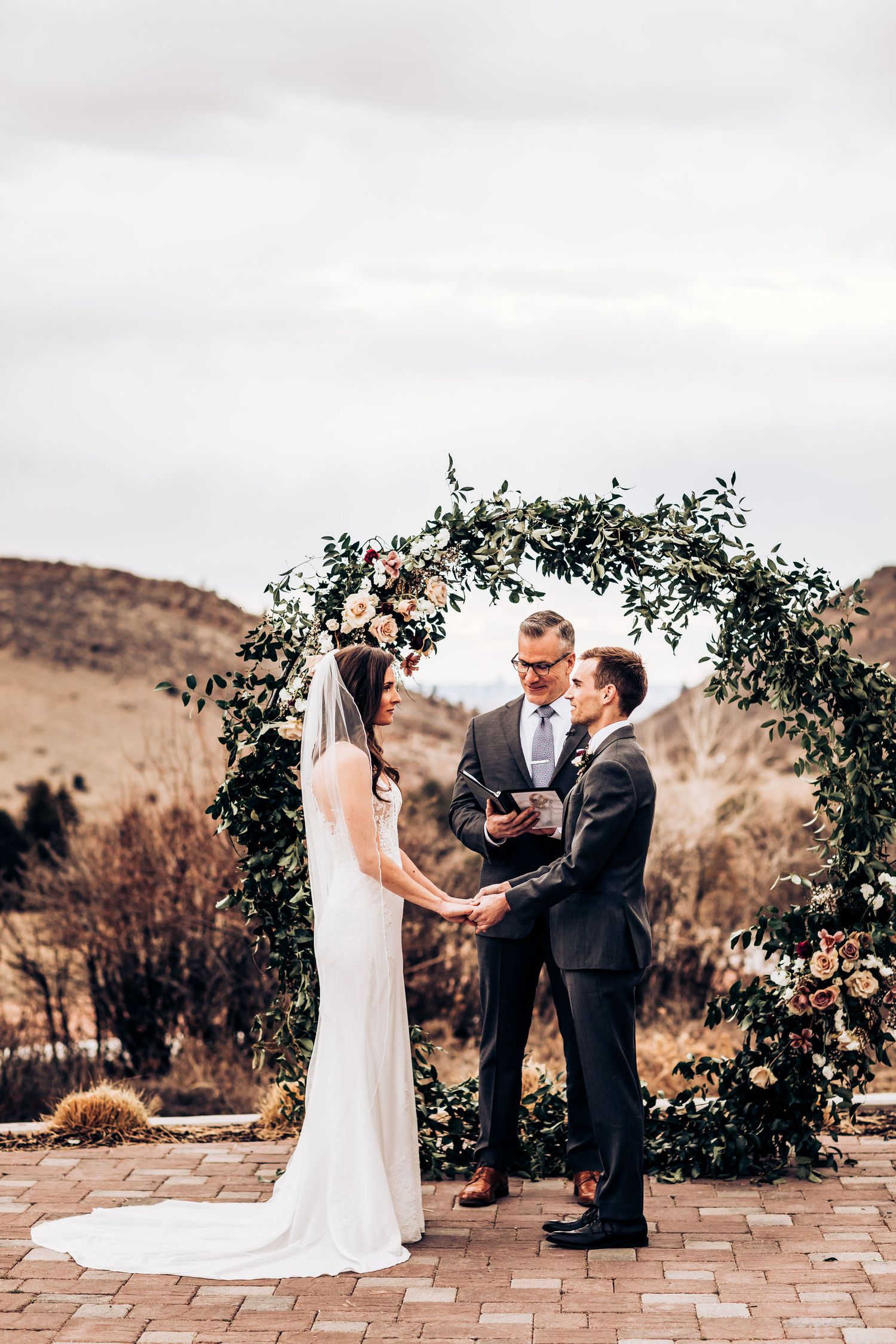 Elegant outdoor wedding ceremony beneath an arch adorned with greenery and blush flowers.