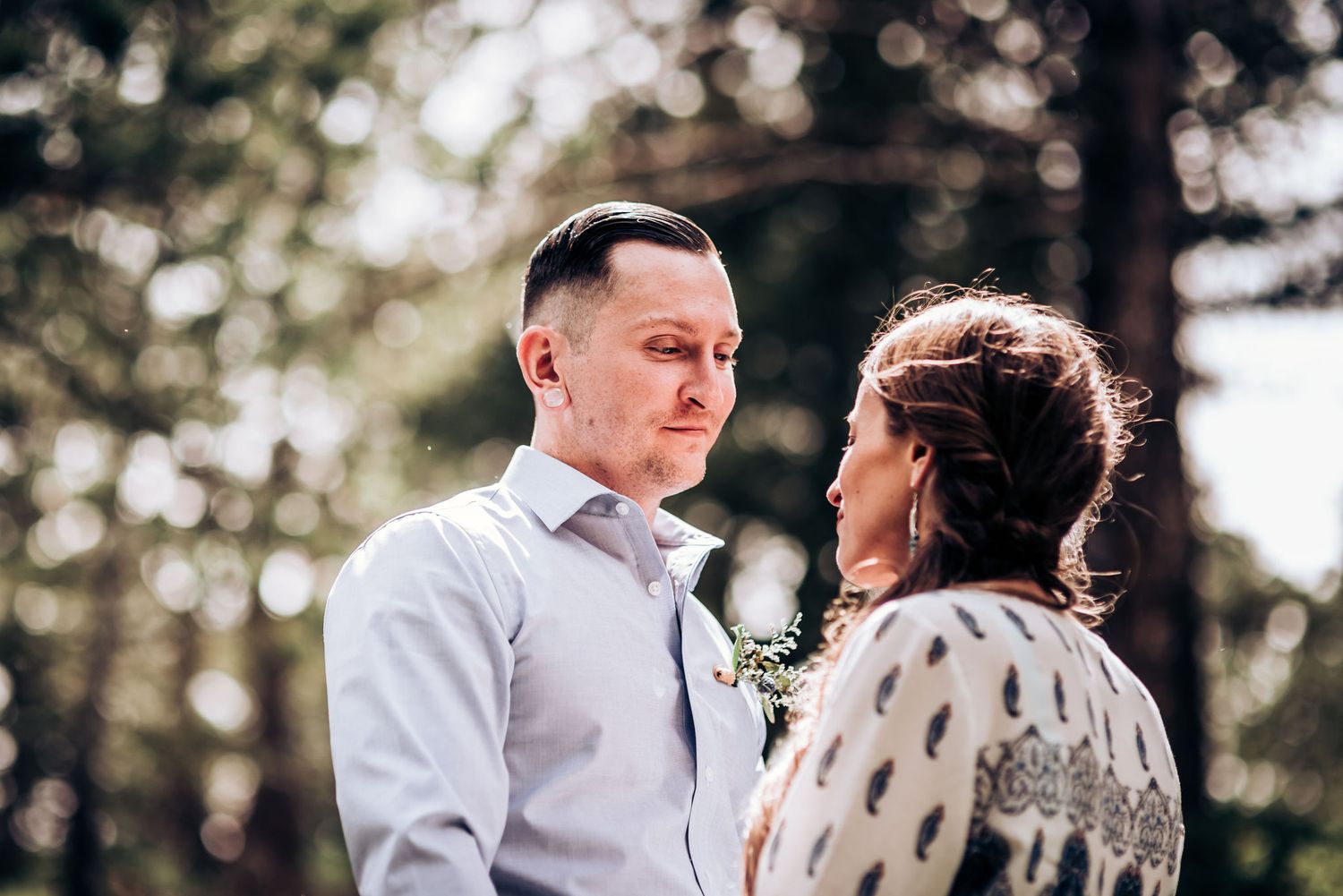 A tender moment shared between a couple in a sun-dappled forest setting.