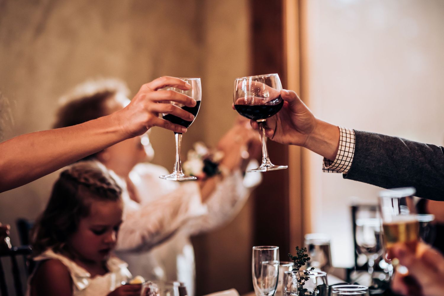 Guests toasting with red wine glasses during elegant wedding reception.