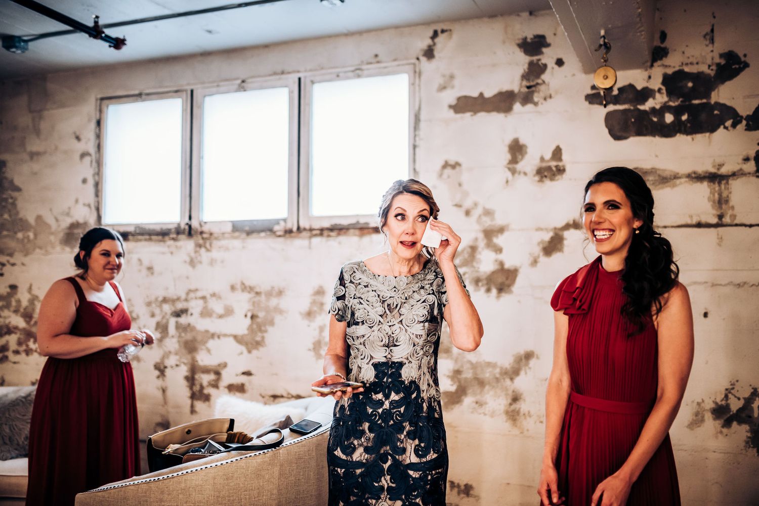 Wedding party members sharing emotional moment in industrial-style venue with exposed walls.